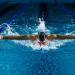 Swimmer performing butterfly stroke in a competitive race at Commonwealth Games.