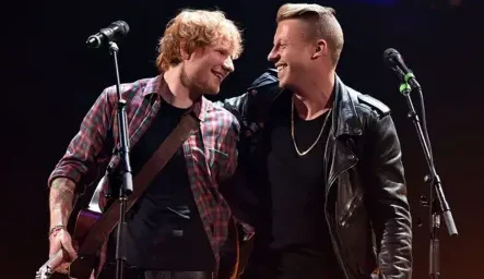 Getty Images Ed Sheeran and Macklemore on stage, in an embrace, during a performance, smiling at each other.